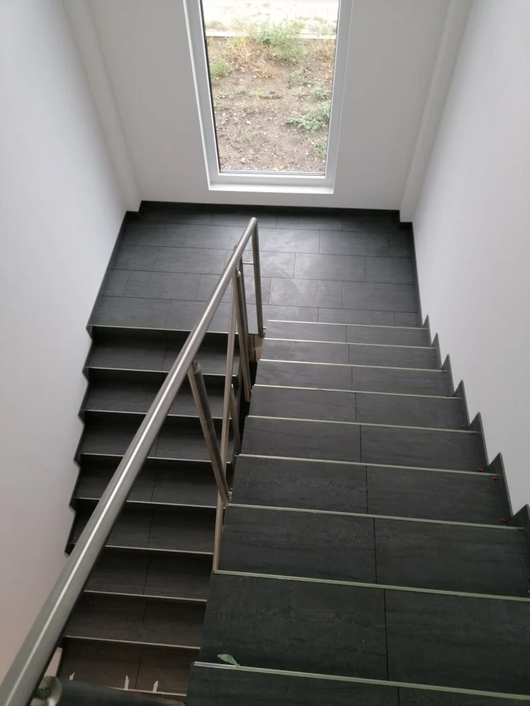 Treppenhaus mit dunklen Fliesen und Edelstahlgeländer